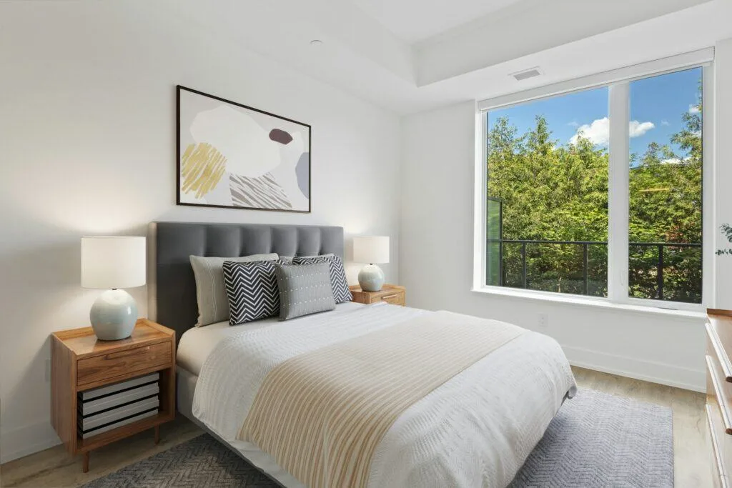 Zero Dry Time A modern bedroom with a neatly made bed, two wooden nightstands with lamps, abstract wall art, and a large window overlooking green trees.